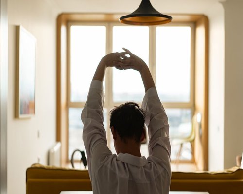 A person taking a standing stretch break by a sunny office window